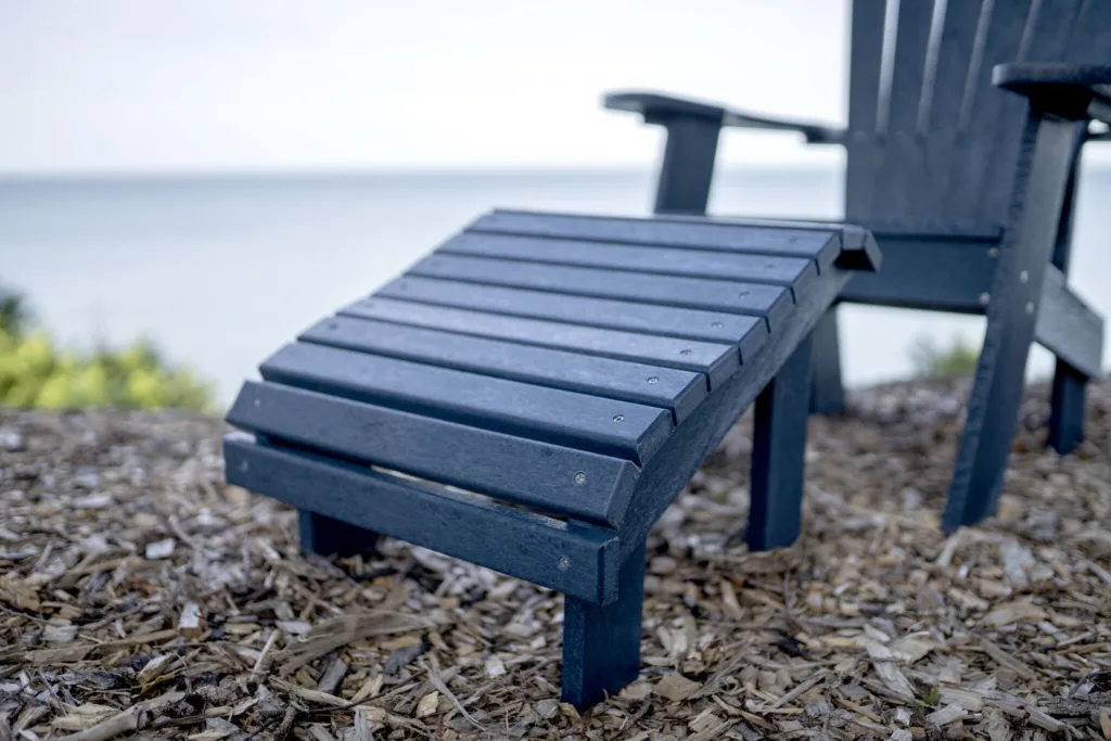 Up close of a Navy Generations Premium Adirondack Footrest in front of a Adirondack chair on the coast