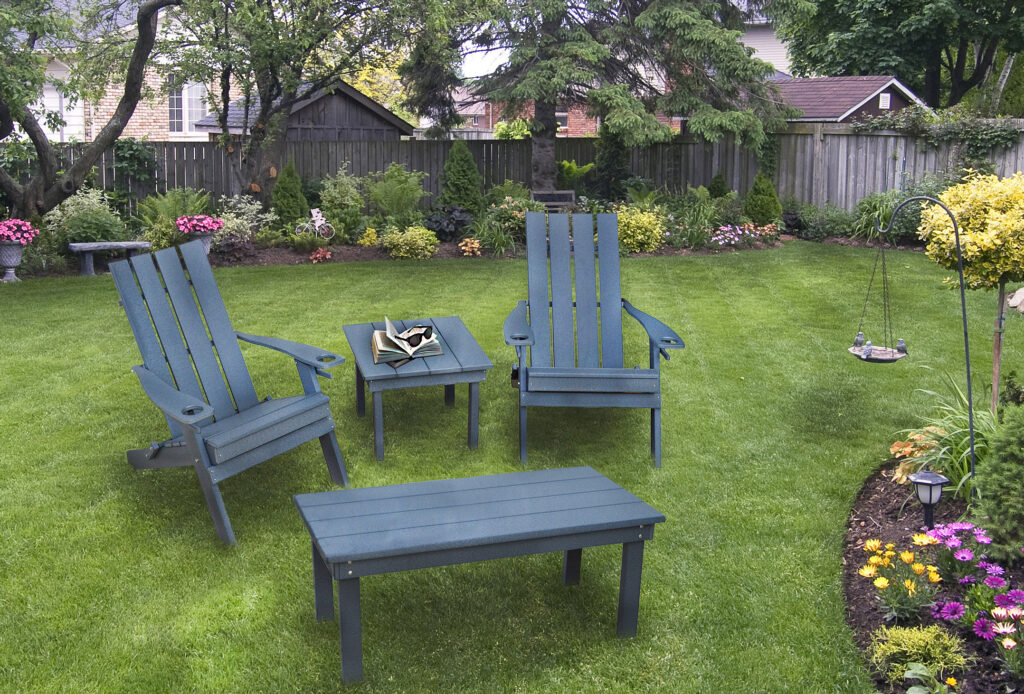 Dark Gray Hampton Folding Adirondack Chairs beside a table on the lawn